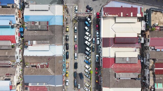 Top-down aerial view of parked cars in Cheras district in Kuala Lumpur, Malaysia. Dense urban layout with colorful rooftops, street activity, and a local commercial area.