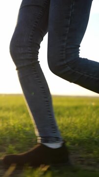 A woman runs swiftly across a grassy field. Her denim jeans feature distinct patterns while the sunlight highlights her movements.