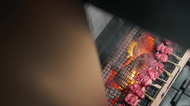 Flames reach up toward a grill full of wagyu beef skewers (slow motion 4K).