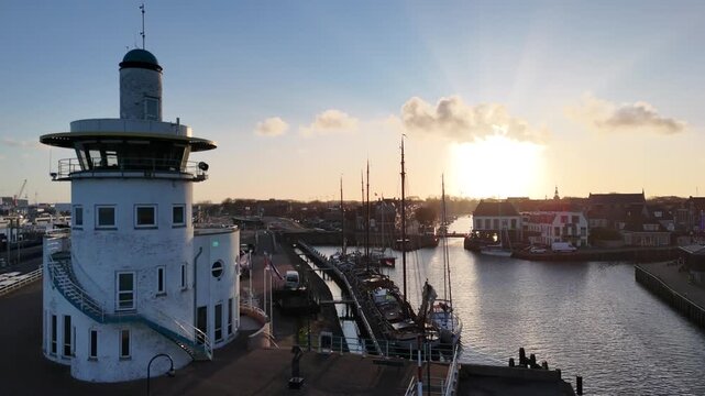 Static sunrise frame of the round harbor control building with flags and sun rays.