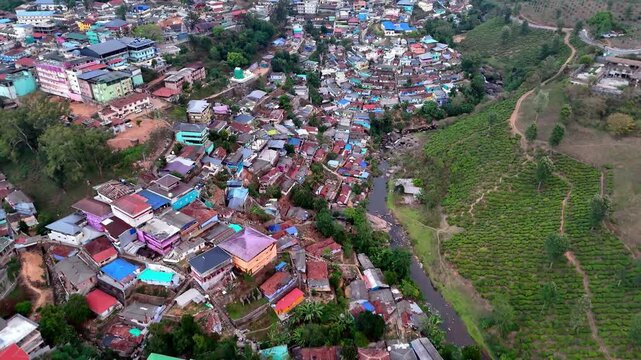 Drone footage moving forward across a vibrant area near Munnar town, transitioning from dense buildings to expansive green hills, with layered terrain and soft haze adding depth and motion.
