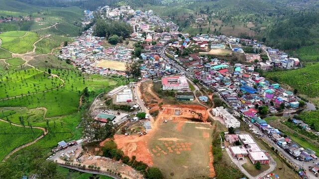 Wide cinematic aerial of Valparai highlighting textured plantations, Lake, and interconnected roads blending into a vast, green mountainous terrain. Hillside town showcasing colorful rooftops.