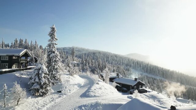 Aerial glide past misty mountain cabins in fresh snowfall and golden morning light, Valdres, Norway.