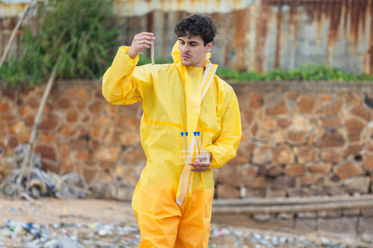 Male researcher in protective gear analyzing water or soil samples at a polluted site, Environmental scientist holding test tubes while conducting field research in a hazardous area