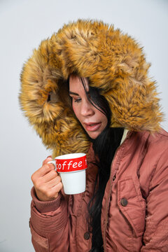 Frau mit Winterjacke und Fellkapuze trinkt Kaffee &ndash; K&auml;lte, W&auml;rme, Lifestyle, Genuss, Herbst Winter, gem&uuml;tlich, Portr&auml;t, Studio, Copyspace, isoliert, freigestellt