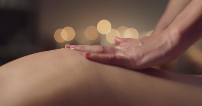 Massage hands on back client therapist relaxation. Soft spa candles form warm bokeh as strokes apply oil and pressure for therapy, easing tension. Concept of soothing bodywork for wellness.