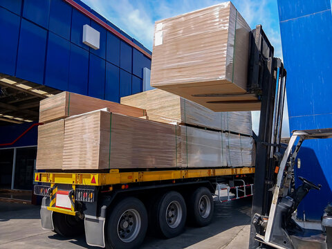 Forklift loading stacks of plywood, PB and HDF boards. Unloading from the truck for storage in the warehouse. Industrial logistics, construction materials supply chain, and wood distribution concept.