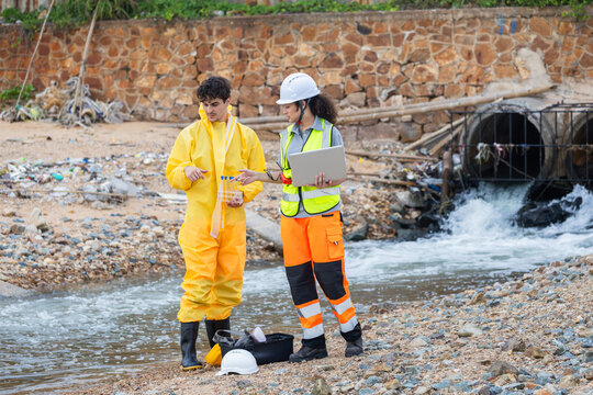 Technical specialist in hazard suit examining liquid samples at a coastal industrial site, Environmentalist in yellow hazmat suit checking water sample near industrial plant