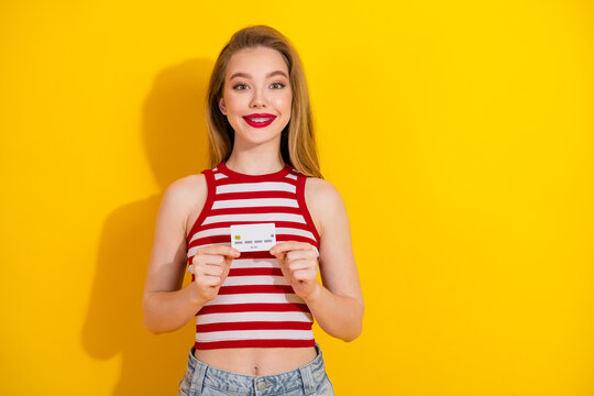Cheerful young woman holding a credit card showcasing vibrant style with a casual striped top against a yellow background