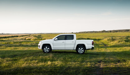 White four-door pickup truck in a summer field. Side profile view of white crew cab truck in a lush green meadow under a clear, late afternoon sky. © andrbk