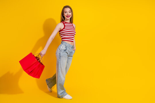 Young woman holding red shopping bags confidently against yellow background, vibrant fashion and holiday sale concept