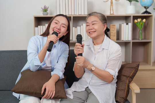 Asian mother and daughter singing karaoke, having fun together at home