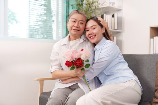 Asian mother and daughter hugging, holding flowers for Mother's Day at home
