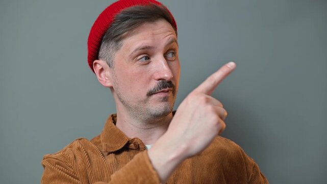 A man wearing a red beanie and brown jacket points in various directions while maintaining a neutral expression