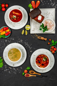 Traditional red borscht and assorted soups with rye bread. Selection of hot soups including borscht with lard and solyanka on a black stone surface.