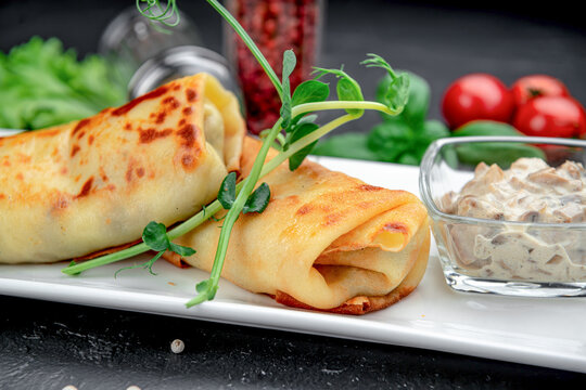 Close up of savory stuffed pancakes with mushroom dip. Angled close up shot of rolled savory crepes garnished with pea shoots and mushroom cream sauce in a glass bowl.