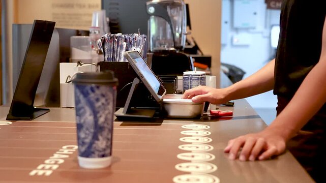 Asian Cashier Using POS Tablet System at a Modern Coffee Shop Counter