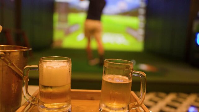 Person Holding Beer Mug in Front of Indoor Golf Simulator