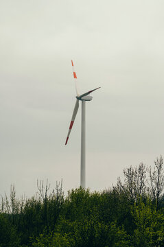 Solitary Wind Turbine Above Green Treeline Muted Overcast Sky, Single Blade Paused Midrotation, Tall White