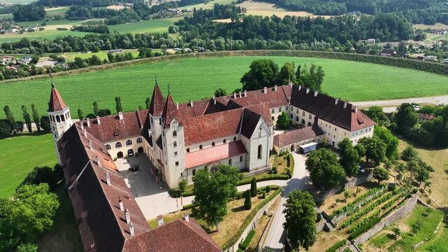 Aerial summer scenery of Sankt Paul im Lavanttal with monastery complex, rooftops, valley landscape, green hills, calm cinematic drone movement, warm atmospheric tones