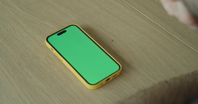 Smartphone with green screen on a table, ideal for screen replacement, app demos, and digital presentations.