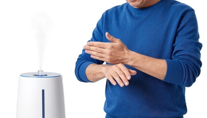Naklejka premium Man in blue sweater warming his hands near a white humidifier emitting cool mist