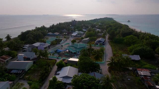 Cinematic aerial drone footage orbiting around the mosque of Vashafaru Island surrounded by tropical homes, palm trees and island scenery in northern Maldives.