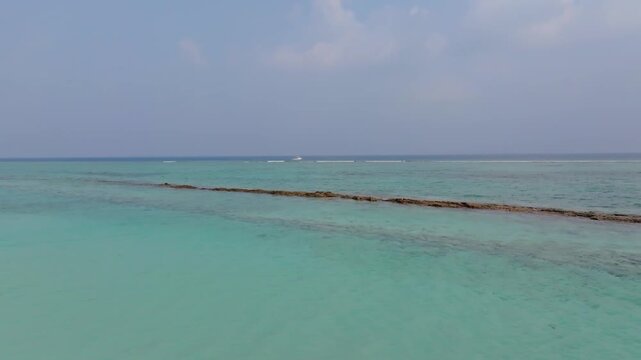 Scenic aerial drone footage flying from the beach of Vashafaru Island across the coral reef and turquoise waters out to a dive boat in northern Maldives.