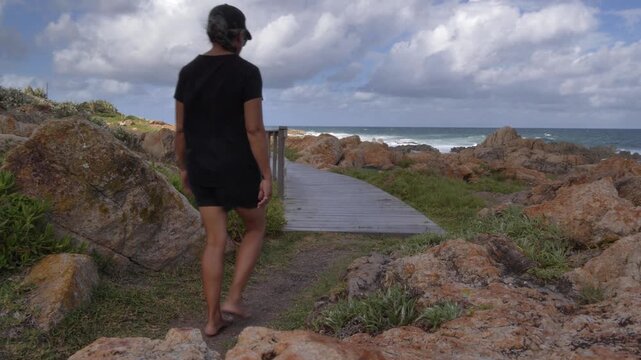 The scene shifts from light to shade as a woman dressed in black strolls along a scenic coastal path, enjoying the rugged landscape and the sound of the sea at Ramsgate, South Coast, KZN.