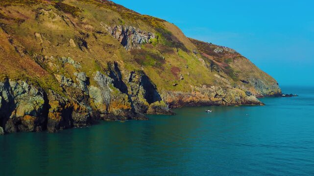Howth Cliffs with Calm Blue Sea, Boat Near Shore and Hikers Walking Along Coastal Trail