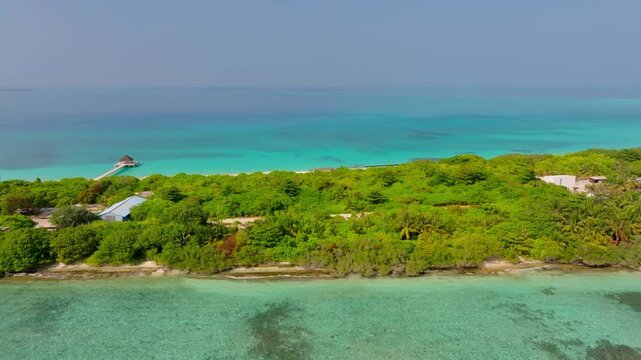 Scenic aerial drone footage flying parallel to the coastline of Vashafaru Island above dense tropical jungle with turquoise ocean waters beside it in northern Maldives.