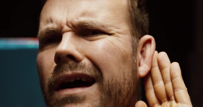 Close-up of a man holding his ear, showing difficulty hearing, confusion, and communication challenge.