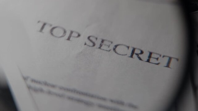Top secret document close up on office desk with magnifying glass. Military or government spy agency report file with sensitive private information or surveillance intelligence. Archive research