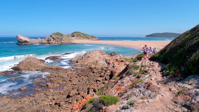 People hike on Robberg circular trail with view of The Island and tombolo beach