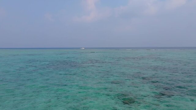 Scenic aerial drone footage approaching from the coast of Vashafaru Island over the coral reef and passing a dive boat in the turquoise waters of northern Maldives.