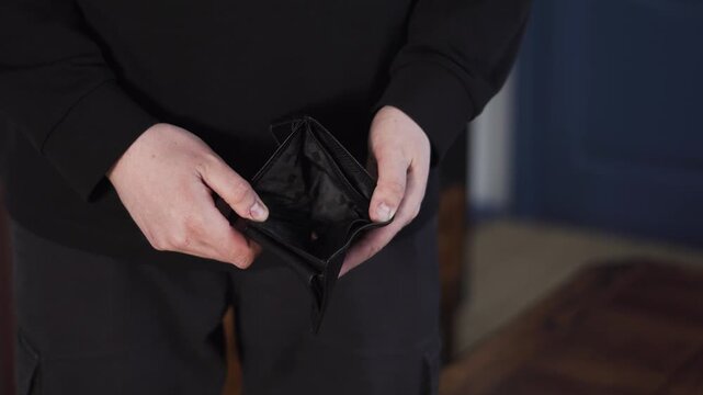 Broke man opens an empty wallet with no cash, showing financial crisis, debt, and money shortage in a close up view.