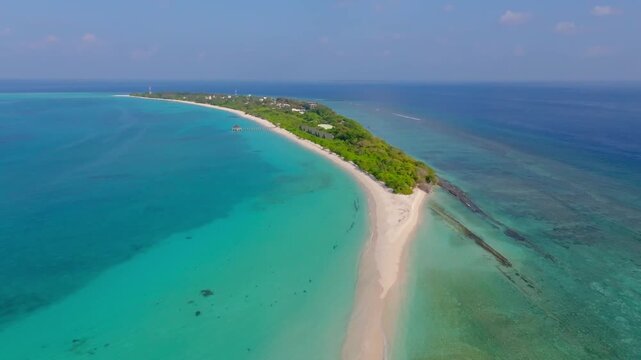 Beautiful aerial drone footage flying parallel to Vashafaru Island from the western side, showcasing a stunning white sand beach and crystal clear turquoise waters in northern Maldives.