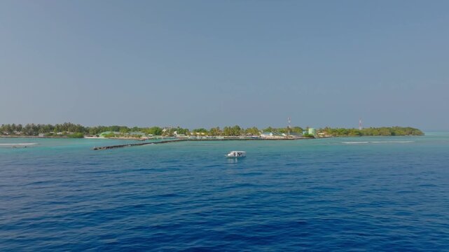 Smooth low aerial drone footage flying from the open ocean over the southern harbor of Vashafaru Island across palm trees to the white northern beach in Maldives