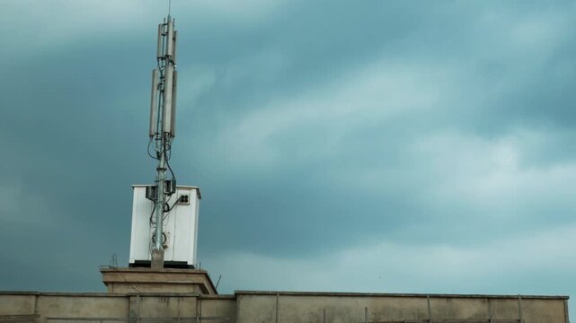 Mobile phone mast and base station located on a city rooftop against a grey overcast sky in Yaound&eacute;, Cameroon. Low angle view.