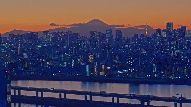 A cinematic telephoto shot showcasing the Tokyo skyline and Tokyo Tower under a vibrant orange sky. Mount Fuji stands majestically in the background while the camera slowly zooms in on the urban archi