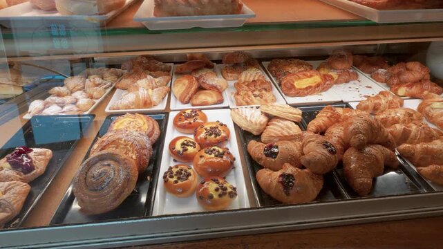 Wide angle shot of a bakery display case filled with golden croissants, danishes, sweet rolls, and pastries under warm lighting, highlighting variety, textures, and inviting freshness. 198 characters.