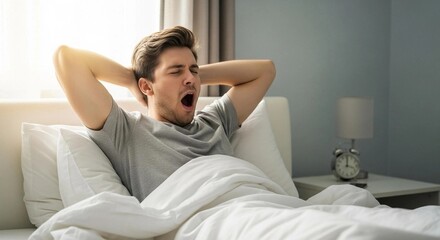 Fototapeta premium Young man yawning and stretching while waking up in a bright bedroom in the morning
