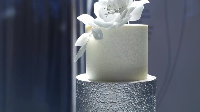 Close-up of a white and silver wedding cake with flowers on a table in a restaurant, illuminated by floodlights. A wedding celebration.