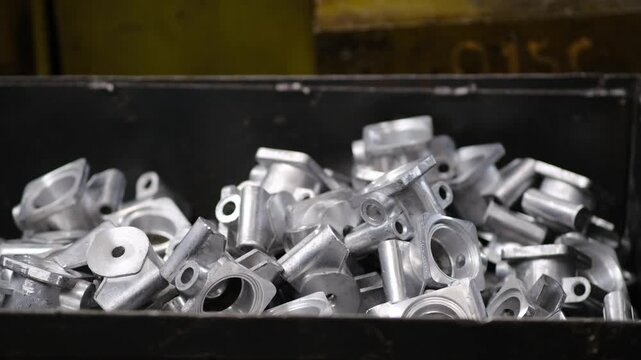 A black metal box full of shiny manufactured aluminum components ready for quality control or further assembly in a plant.