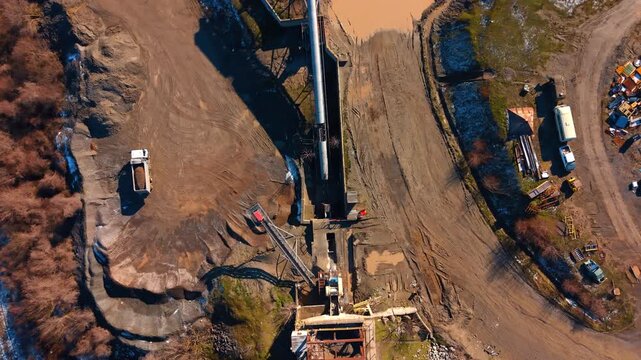Site displays tools and materials. Heavy machinery and vehicles are on a construction site with dirt and water puddles present, showing ongoing work.