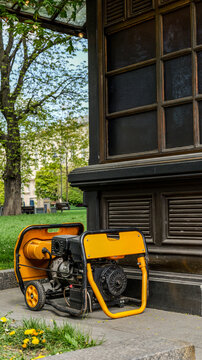 Portable yellow generator sits on pavement near a dark building and green lawn