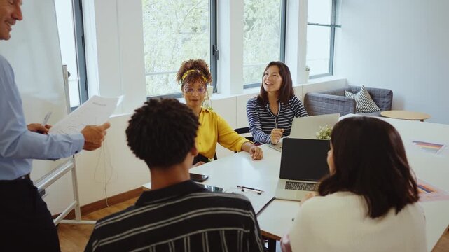 Multicultural business people brainstorming and talking about a new project during a briefing, analyzing data and charts on papers and laptops in a bright and modern conference room