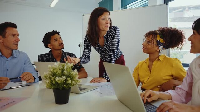 Multicultural business people brainstorming and talking about a new project during a briefing, analyzing data and charts on papers and laptops in a bright and modern conference room