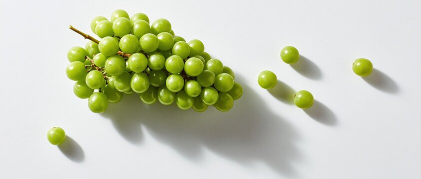 Green grapes flat lay on white background with scattered berries and long shadows, minimal food concept with copy space for healthy eating designs.
