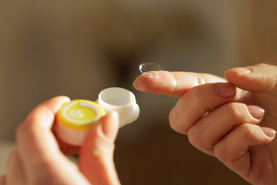 Contact lens on fingertip with open case for vision correction and eye care routine